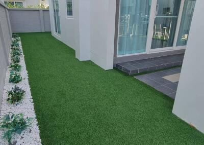 View of a yard with artificial grass and a flower bed.