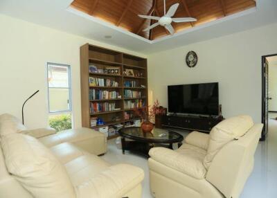 Cozy living room with cream leather sofas, ceiling fan, large bookshelf, TV, and glass coffee table