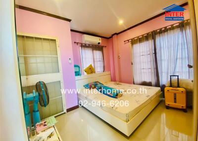 Bright bedroom with bed, air conditioner, standing fan, and luggage