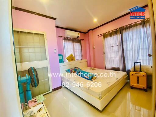 Bright bedroom with bed, air conditioner, standing fan, and luggage