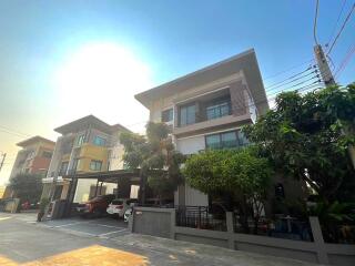 Three-story modern residential building with covered parking area and surrounding greenery