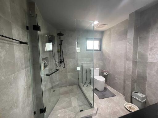 Modern bathroom with a glass-enclosed shower, toilet, and small window