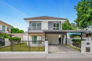 Exterior view of a modern two-story house with a carport and surrounding greenery