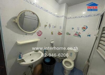 Bathroom with white tile walls, circular mirror, sink, toilet, and child-themed wall decals