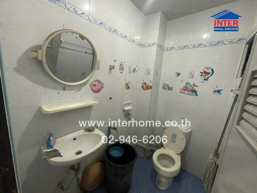 Bathroom with white tile walls, circular mirror, sink, toilet, and child-themed wall decals