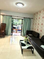 Living room with glass door opening to outdoor area, featuring a couch, rocking chair, coffee table with flowers, and tiled floor