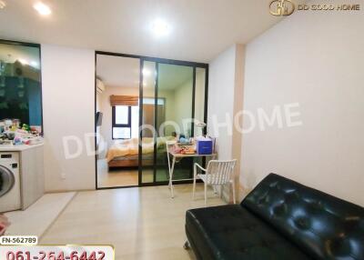 Living area with a black sofa and glass partition showing bedroom