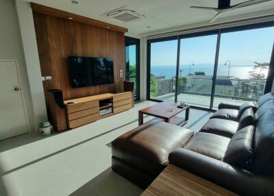 Modern living room with brown leather sofa and wooden TV stand, large windows with ocean view