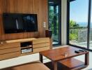 Modern living room with wooden wall, large TV, and glass doors to a balcony with sea view