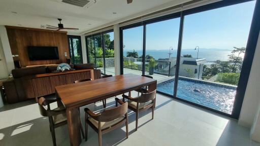 Bright living area with glass doors leading to a pool and ocean view, featuring wooden dining set and TV