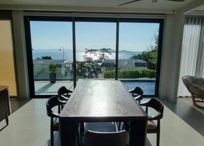 Dining room with a large wooden table and chairs, overlooking a scenic ocean view