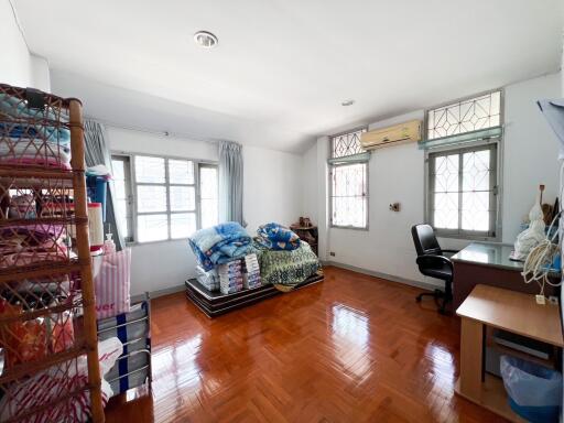 A spacious bedroom with large windows, wooden flooring, a bed, a desk, and shelves.