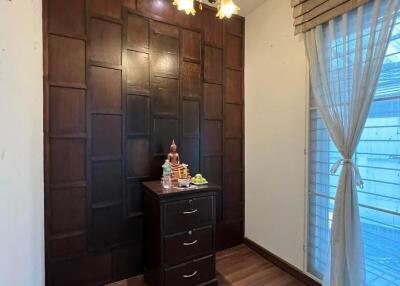 Small bedroom with wooden floor, dark wood wall panel, chest of drawers, chandelier, and large window with sheer curtains