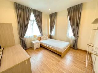 A bright bedroom with large windows, curtains, and wooden furniture