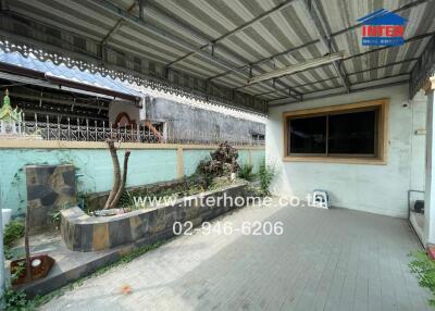 Covered outdoor patio area with paved flooring, garden bed, and wall decor