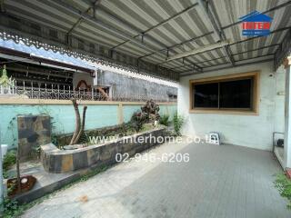 Covered outdoor patio area with paved flooring, garden bed, and wall decor