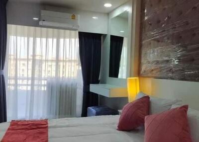 A well-furnished bedroom with double bed, bedside table with lamp, large window with curtains, and air conditioner.