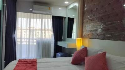 A well-furnished bedroom with double bed, bedside table with lamp, large window with curtains, and air conditioner.