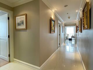 A well-lit corridor with framed paintings and a view towards a bright room.