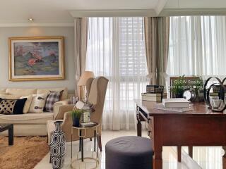 Cozy living room with armchair, couch, and desk next to a large window with sheer curtains