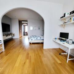 Spacious bedroom with hardwood floors, desk, and large archway