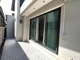 Outdoor view of a modern building exterior with sliding glass doors and a small paved patio area