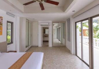 Large, well-lit bedroom with glass doors leading to a balcony, a ceiling fan, and mirrored closets.