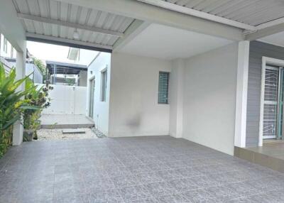 A spacious carport with tiled flooring and nearby greenery.