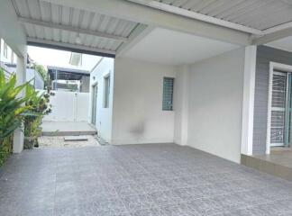 A spacious carport with tiled flooring and nearby greenery.