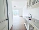 Well-lit kitchen with white cabinetry leading to a bright living area