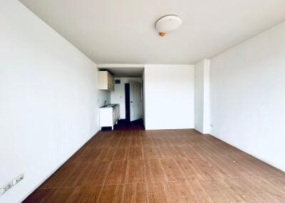 Empty living area with hardwood floors and kitchen in the background