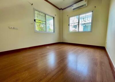 Empty bedroom with wooden flooring, white walls, and two windows with grills