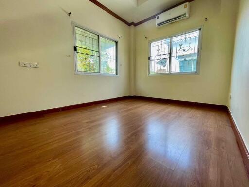 Empty bedroom with wooden flooring, white walls, and two windows with grills