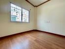 Spacious empty bedroom with wooden flooring and a window