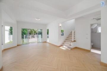 Spacious living room with large windows, wooden flooring, and a staircase.