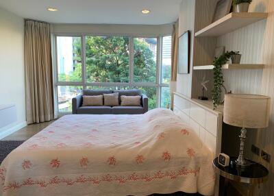 Well-lit bedroom with large windows, double bed, bedside lamp, shelves, a couch, and a tree view