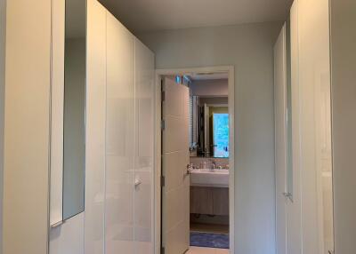 View of a hallway with white wardrobes leading to a bathroom with a vanity mirror