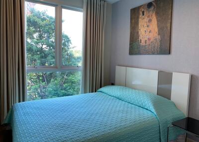 A cozy bedroom with a large window, curtains, a bed with a teal bedspread, and wall art