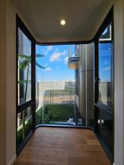 Modern glass-enclosed corridor with wooden flooring, overlooking an exterior with modern architecture