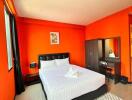 Bright bedroom with orange walls, bed, wardrobe, and desk