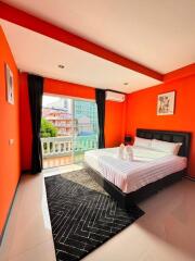 Modern bedroom with vibrant orange walls, a large bed, and a balcony view