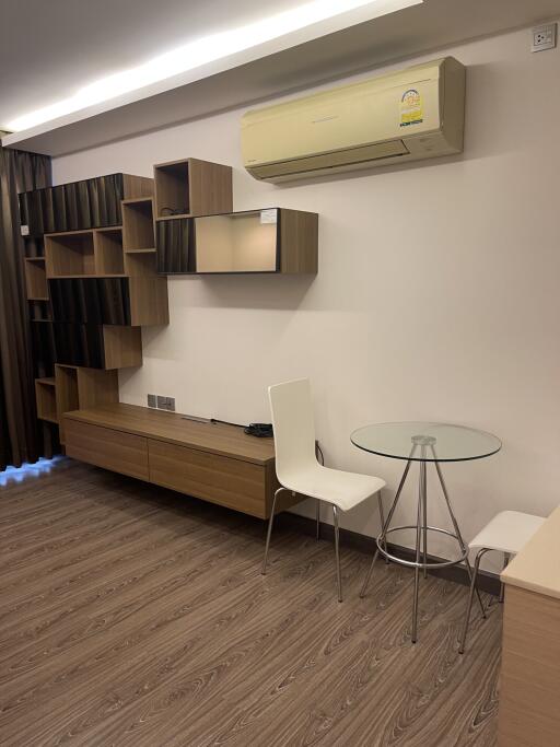 Modern living room with wooden flooring, wall-mounted shelves, air conditioning, and minimalist furniture