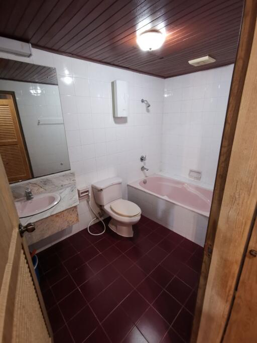 Bathroom with white tile walls, a bathtub, toilet, sink, and wooden ceiling.