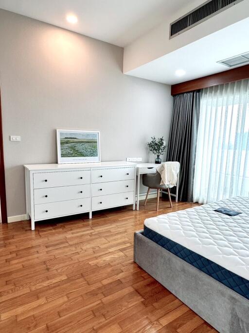 Modern bedroom with wooden flooring, white dresser, and bed