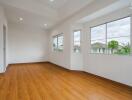 Bright empty bedroom with wooden floor and multiple windows