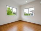 Spacious empty bedroom with wooden flooring and two large windows