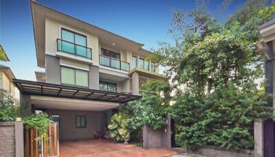 Modern multi-story house with a carport and lush greenery