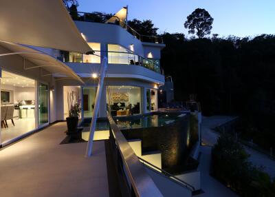 Modern multi-story house with glass balconies and outdoor pool at twilight