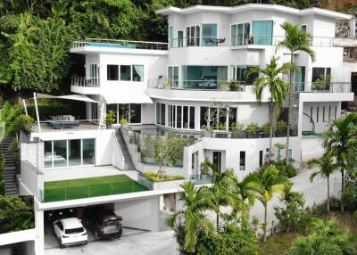 Modern multi-level white house with large windows and tropical greenery