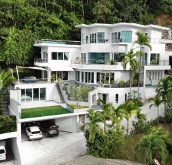 Modern multi-level white house with large windows and tropical greenery